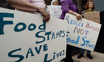 People holding signs with blue writing on white background: "Food stamps save lives" and "Feed People Not Pentagon"
