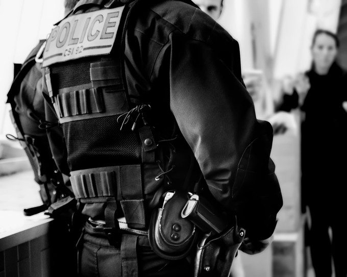 Black and white photo of the back of an officer wearing a vest that reads "Police"
