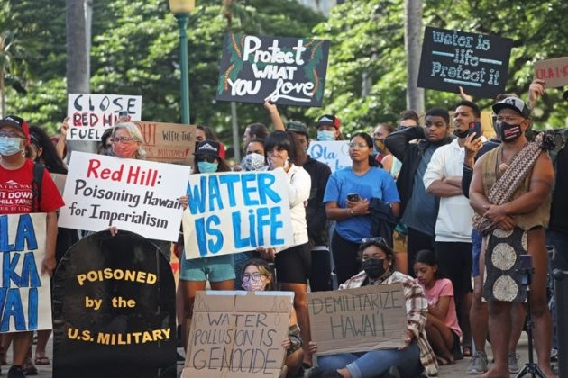 Protesters hold signs saying "water is life" and "poisoned by the U.S. military"